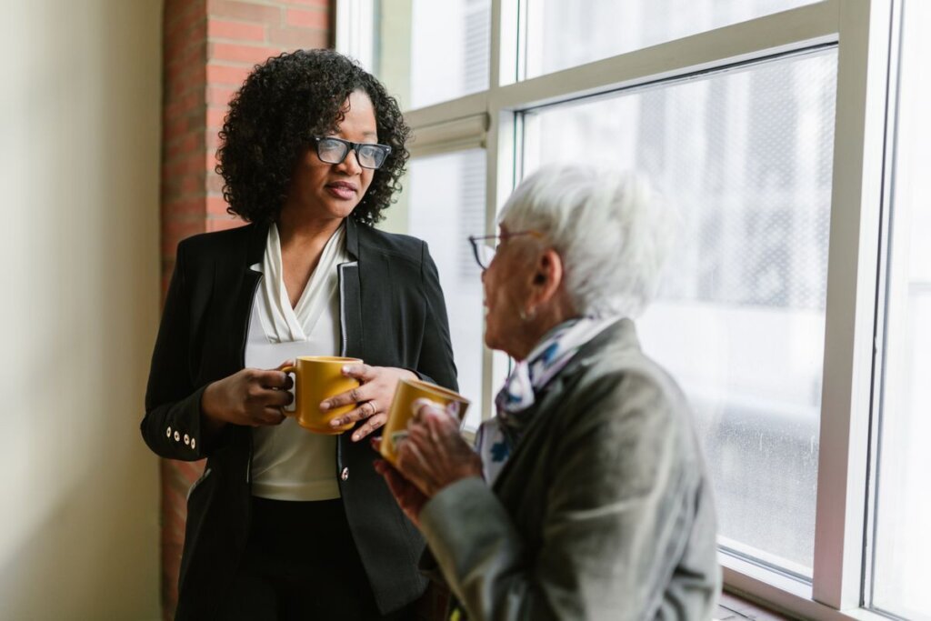 Two women talking over coffee by a window, a mentoring conversation that offers guidance and accountability