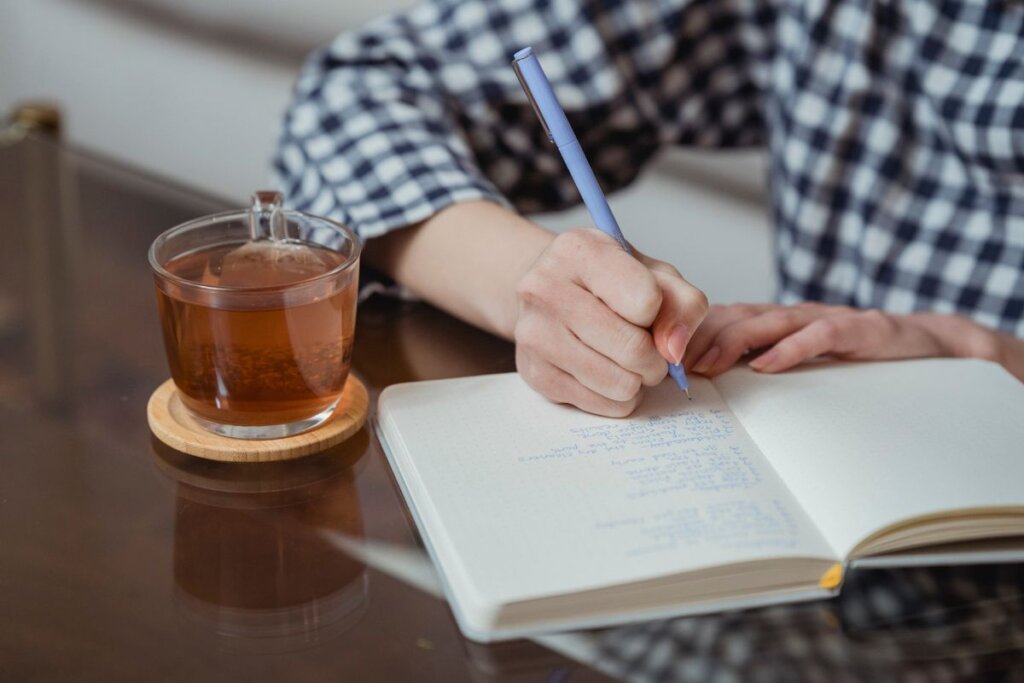 Hands writing in a notebook beside a glass of tea, reflecting on a 90-day personal reset plan