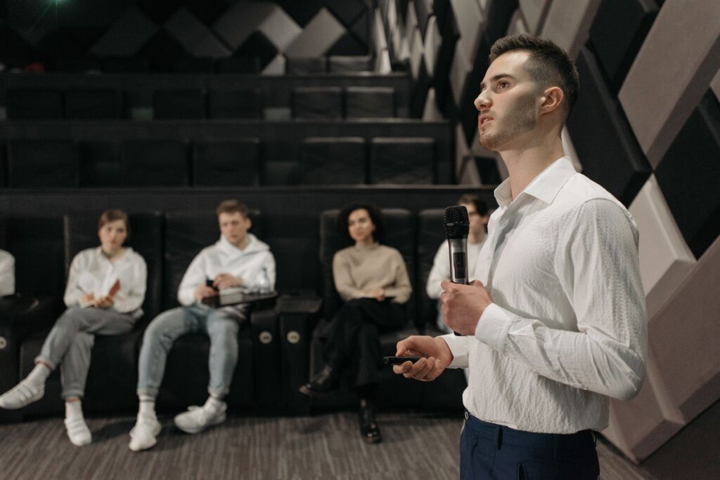 Man holding a microphone and presenting to a small group, practicing confident communication under pressure