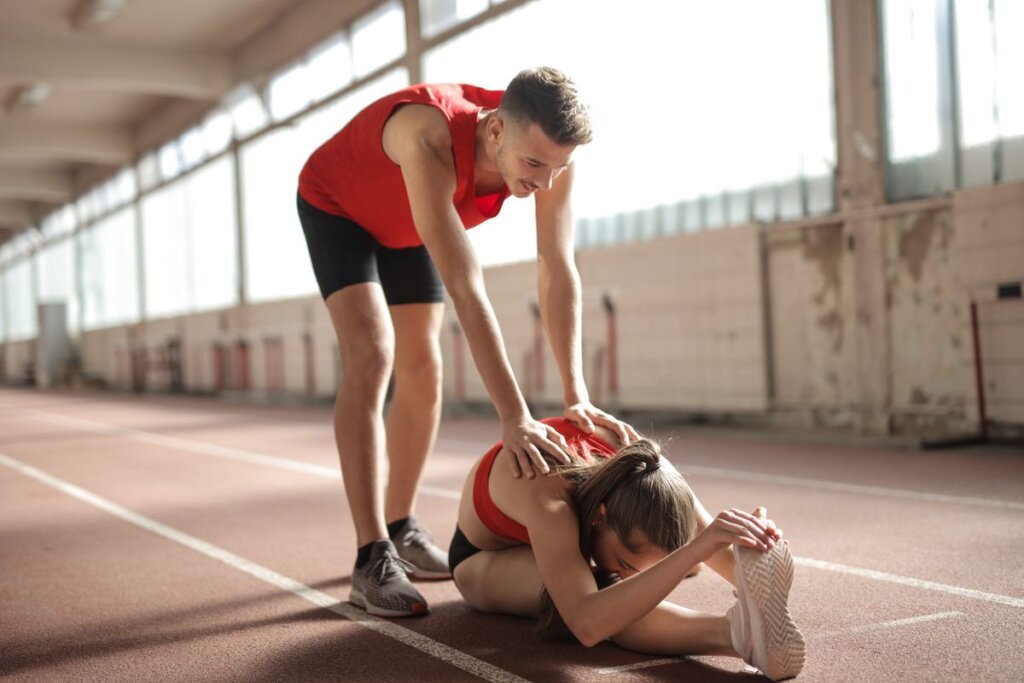 Coach helping an athlete stretch on a running track, showing how guidance improves performance